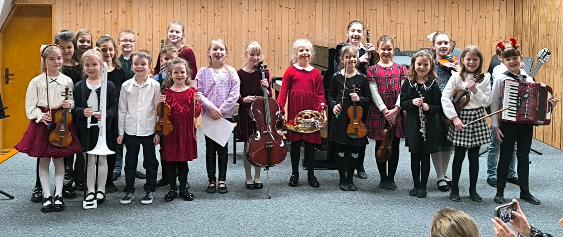 Wszyscy wykonawcy, grupa około dwudziestu dzieci, stoją na scenie ze swoimi instrumentami.