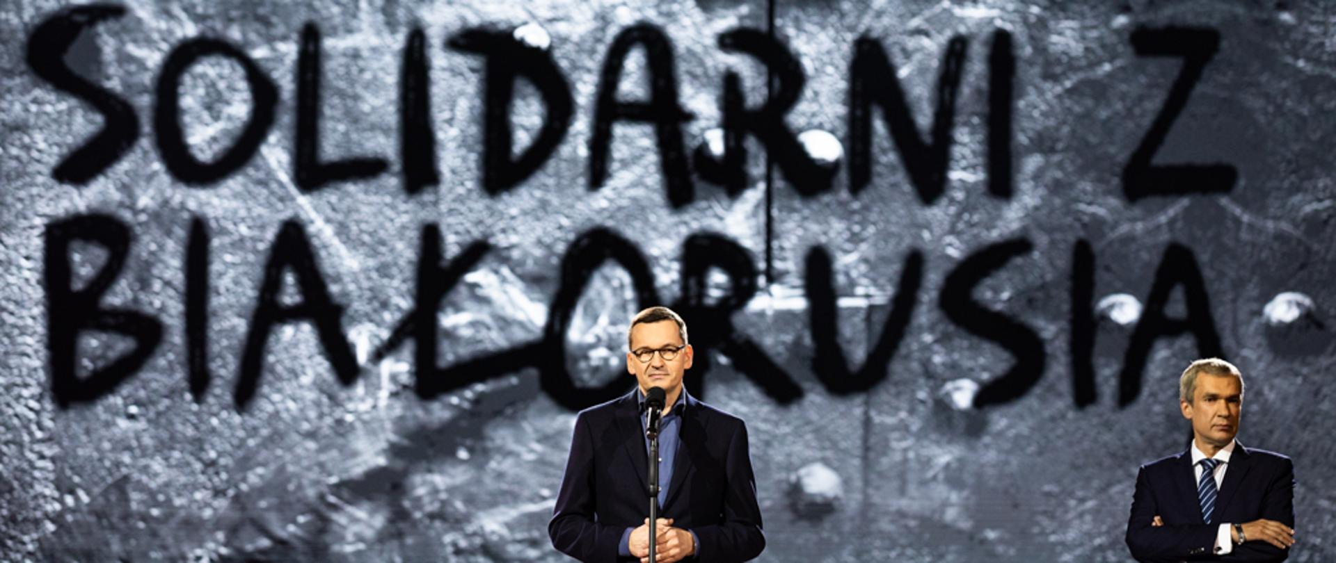 Premier Mateusz Morawiecki przemawia na tle napisu: Solidarni z Białorusią.