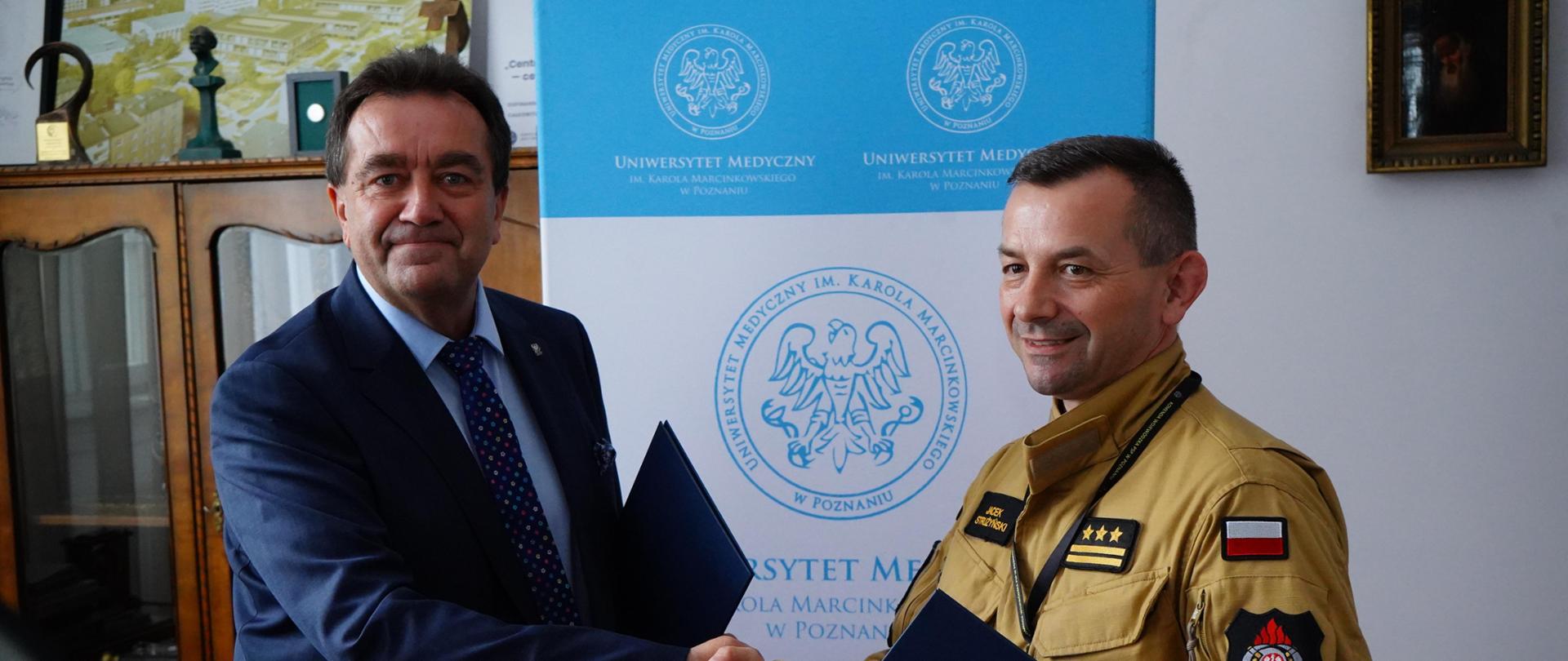 Pan Komendant i Pan Rektor gratulują sobie, wymieniając uścisk dłoni. Stoją.