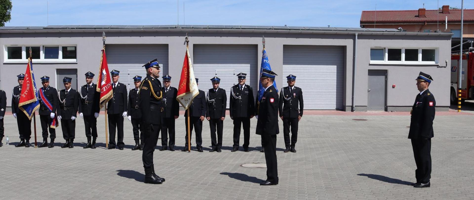 Zdjęcie przedstawia dowódcę uroczystości powiatowych obchodów dnia strażaka, który składa meldunek dla Komendanta Wojewódzkiego PSP w Szczecinie, a także poczty sztandarowe OSP stojące na zbiórce.