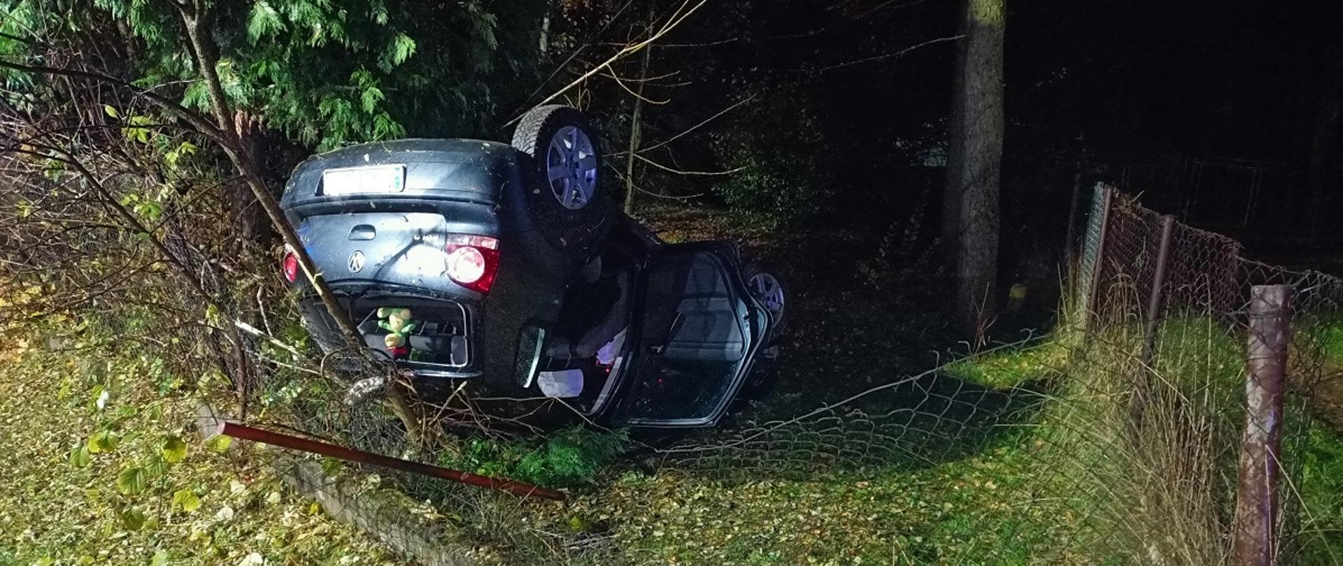 Zdjęcie przedstawia przewrócony samochód na dach poza drogą.