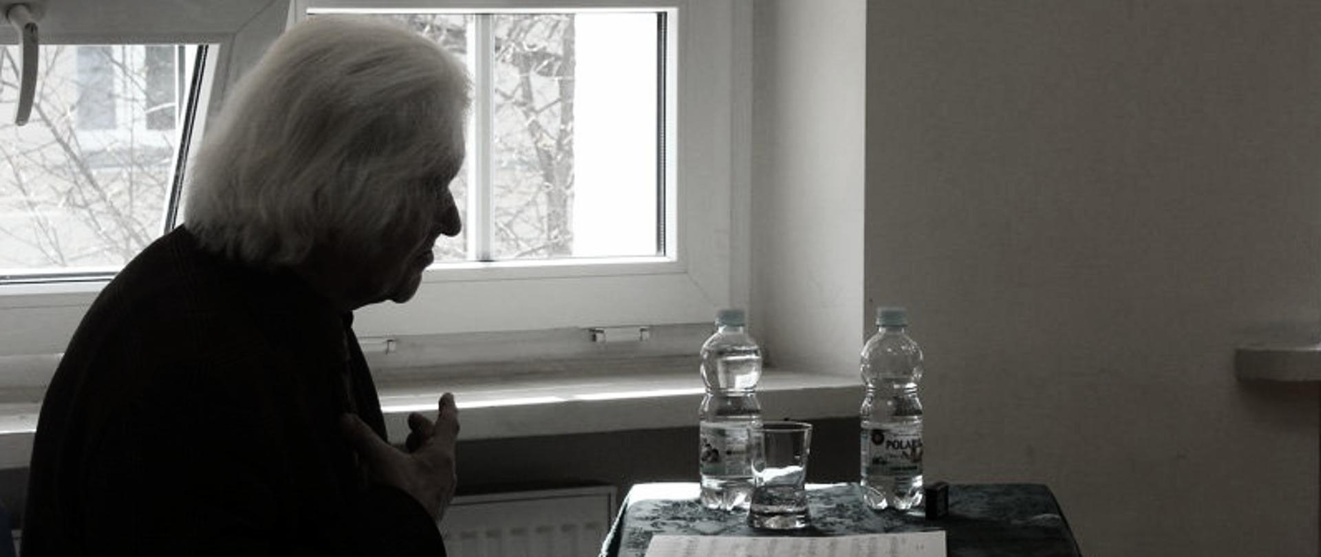 czarno białą fotografia po lewej stronie siwy starszy człowiek siedzący na tle okna