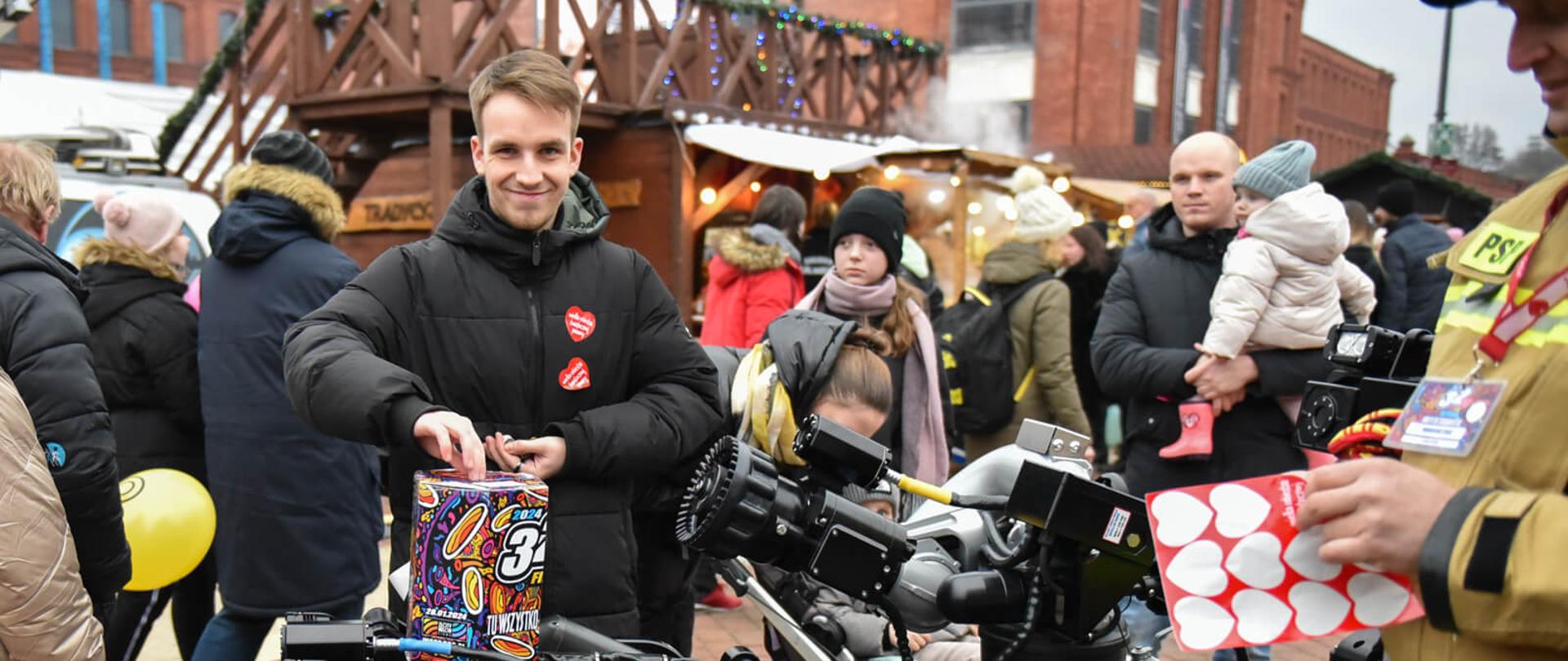 Strażak stojący przy robocie gaśniczym obok mężczyzna wrzucający pieniądze do puszki