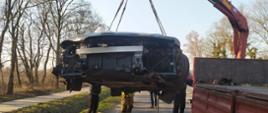 Kolizja drogowa-dachowanie audi. Droga gminna Rawicz-Przywsie. Załadunek rozbitego audi na samochód ciężarowy. Auto ładowane jest za pomocą HDS i pasów transportowych. W tle drzewa.