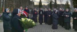 Grupa osób składa znicze i kwiaty na grobie. 