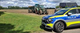 Policyjny radiowóz na tle ciągnika rolniczego. 