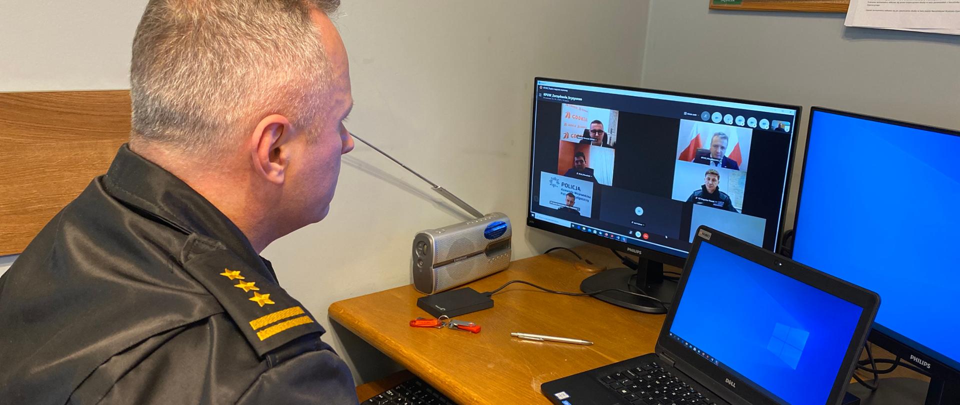 Wideokonferencja - Akcja Zima 2021 - na zdjęciu zastępca kujawsko-pomorskiego komendanta wojewódzkiego st. bryg. Robert Wiśniewski w trakcie zdalnego spotkania Sztabu kryzysowego. Tematem omawianym są warunki zimowe w regionie. Komendant w umundurowaniu dowódczo-sztabowym. Na monitorze widoczni rozmówcy - członkowie Sztabu.
