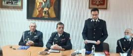 Sala Narad OSP Włoszczowa, stół prezydialny przy którym zasiadają od lewej dh Mirosław Pawlak, st. kpt. Andrzej Pacanowski, dh Bartłomiej Robak (odczytuje sprawozdanie z działalności), dh Wiktor Krotla, w tle ściana z obrazem św. Floriana oraz godło Polski