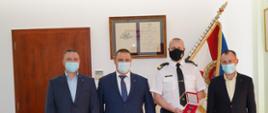 trzech mężczyzn w garniturze oraz strażak stoją przed sztandarem , strażak trzyma w ręku medal.