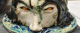 Praca ceramiczna - przedstawia głowę, widzianą od nosa w górę, która wyłania się z wody; w roli wody wykorzystano okrągły krążek, wielkości średniego talerza, na którym znajdują się lekkie fale wody. Praca leży na stole w pracowni