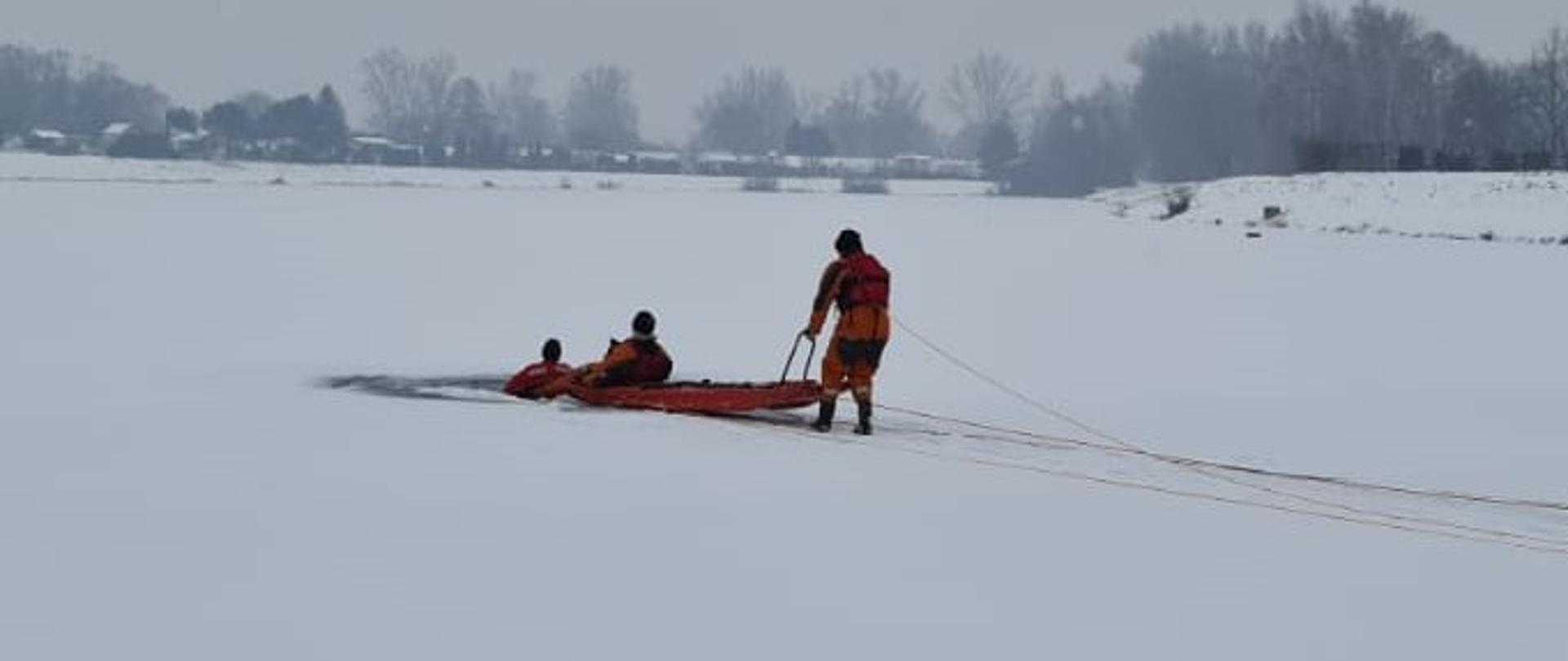 Trzech strażaków na lodzie z saniami do ratowania ludzi. Ćwiczenia z zakresu ratownictwa lodowego. 