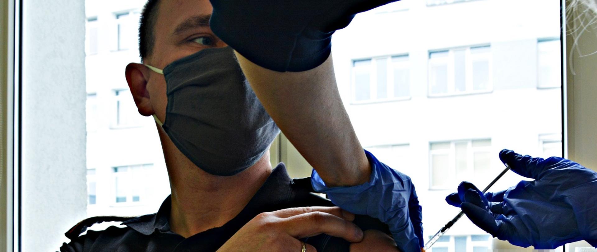 Na zdjęciu widać podawanie w ramię szczepionki dla strażaka.