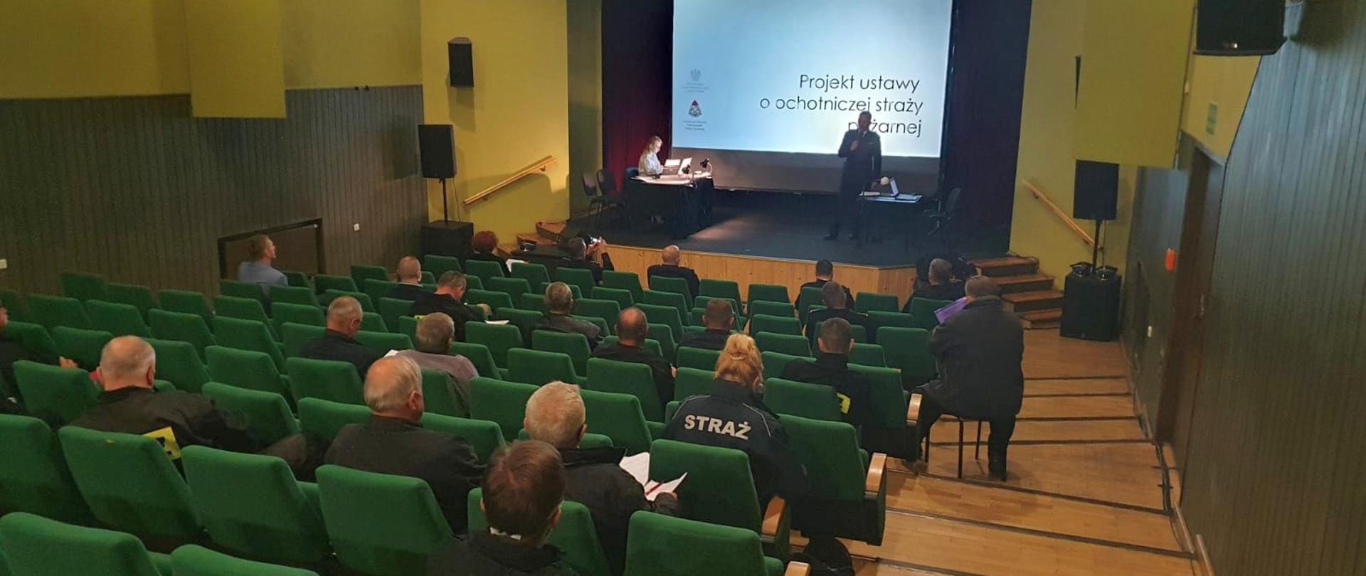 Zdjęcie przedstawia salę w domu kultury na której siedzą strażacy.