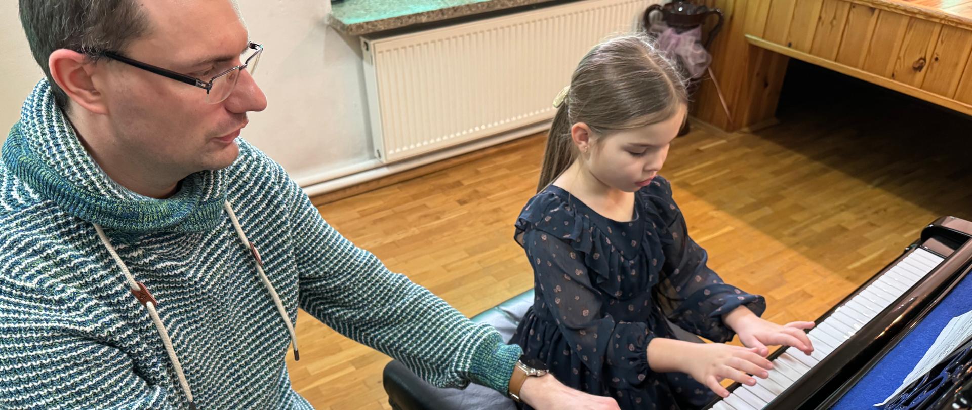 Zdjęcie przestawiające jednego z uczestników warsztatów pianistycznych przy fortepianie, które odbyły się w auli szkoły. Przy uczestniku znajduje się prowadzący warsztaty - dr hab. Gracjan Szymczak.