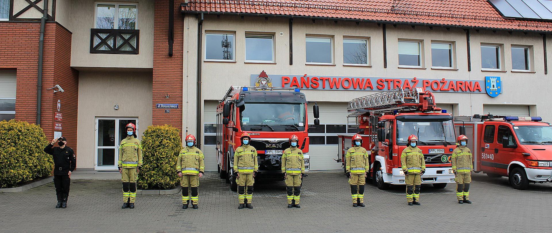 Przed Komendą Powiatową Państwowej Straży Pożarnej w Pleszewie Strażacy w geście solidarności i ku czci poległego policjanta oddają honor. Przed komenda ustawione są samochody pożarnicze, w szeregu stoją Strażacy. 