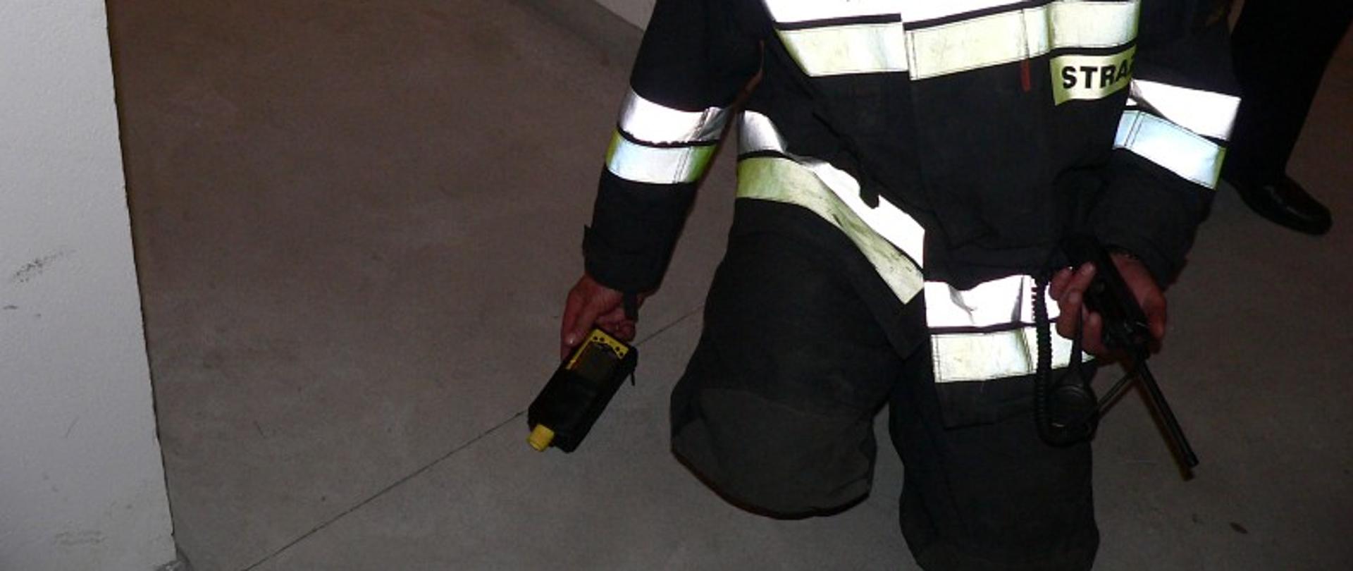 Strażak klęczy na podłodze z urządzeniem pomiarowym w budynku mieszkalnym.