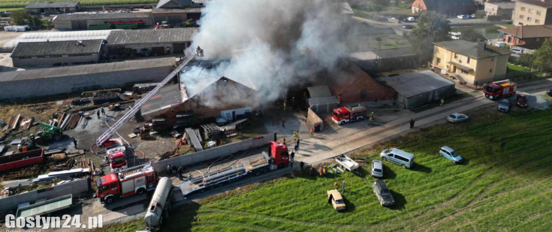 Zdjęcie z drona. Duże zadymienie z budynku. Na zdjęciu są także samochody pożarnicze, samochody cywilne oraz budynki sąsiadujące.