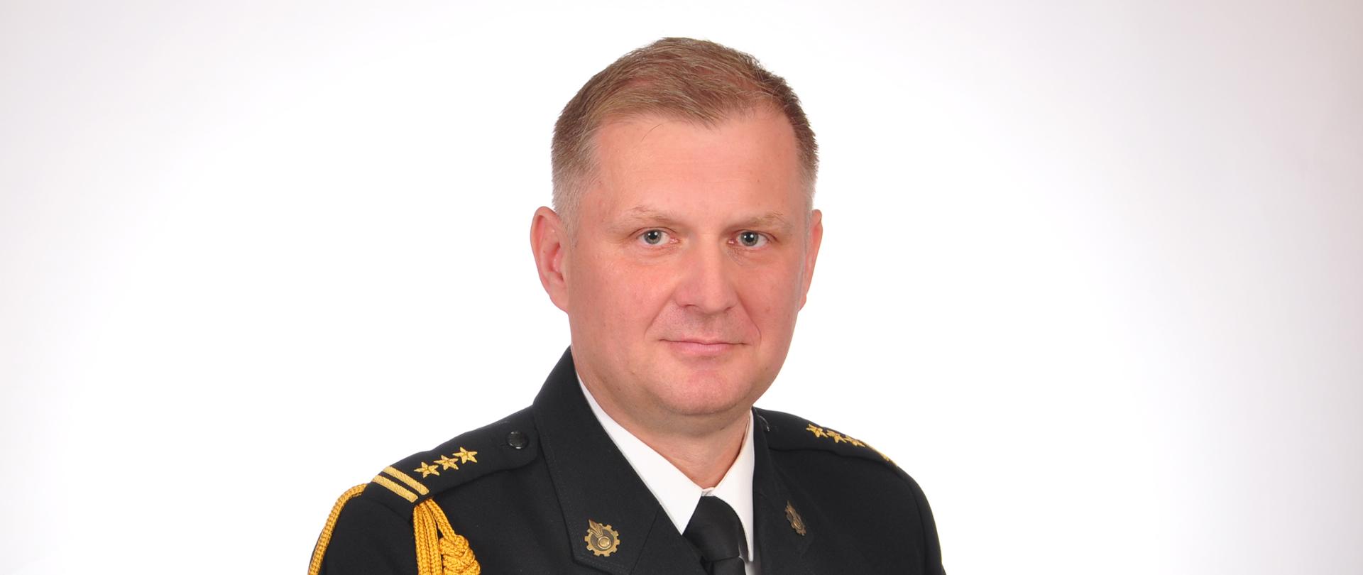 Zdjęcie portretowe st. bryg. mgr inż. Kamila Bieńkowskiego - Komendanta Powiatowego PSP w Kozienicach w mundurze wyjściowym na jasnym tle