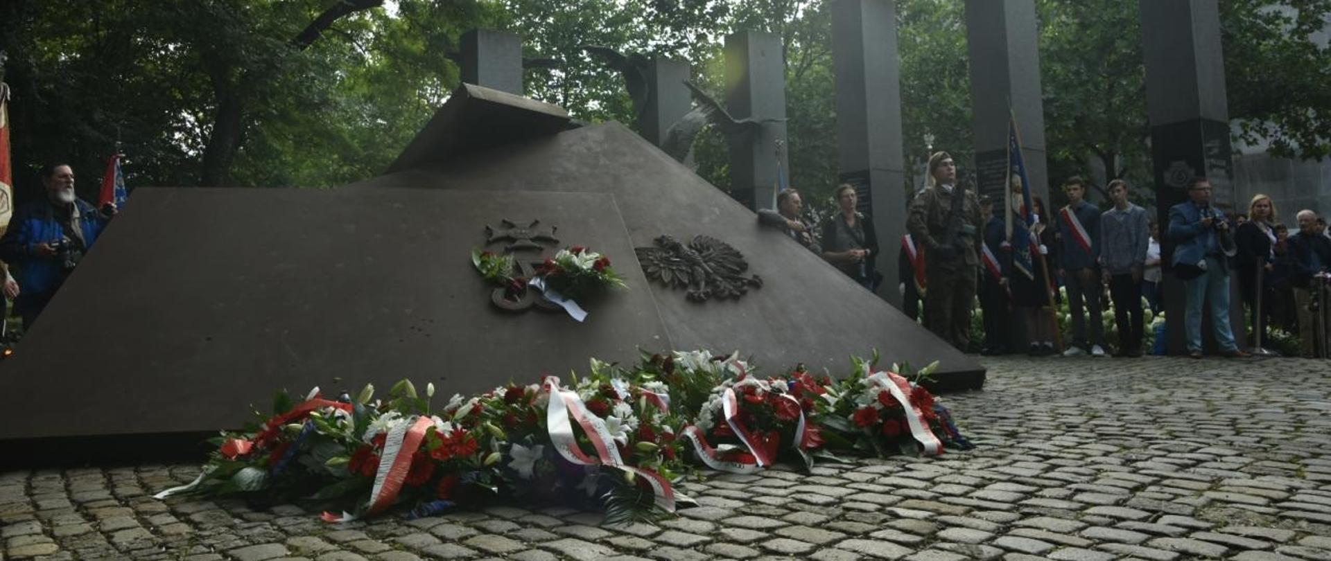 duży pomnik złożony z dwóch płyt żeliwnych, ma jednej z nich znak Polski walczącej a na drugim orła polskiego. przed pomnikiem leżą wiązanki kwiatów z biało czerwonymi szarfami, obok pomnika stoją poczty sztandarowe, 