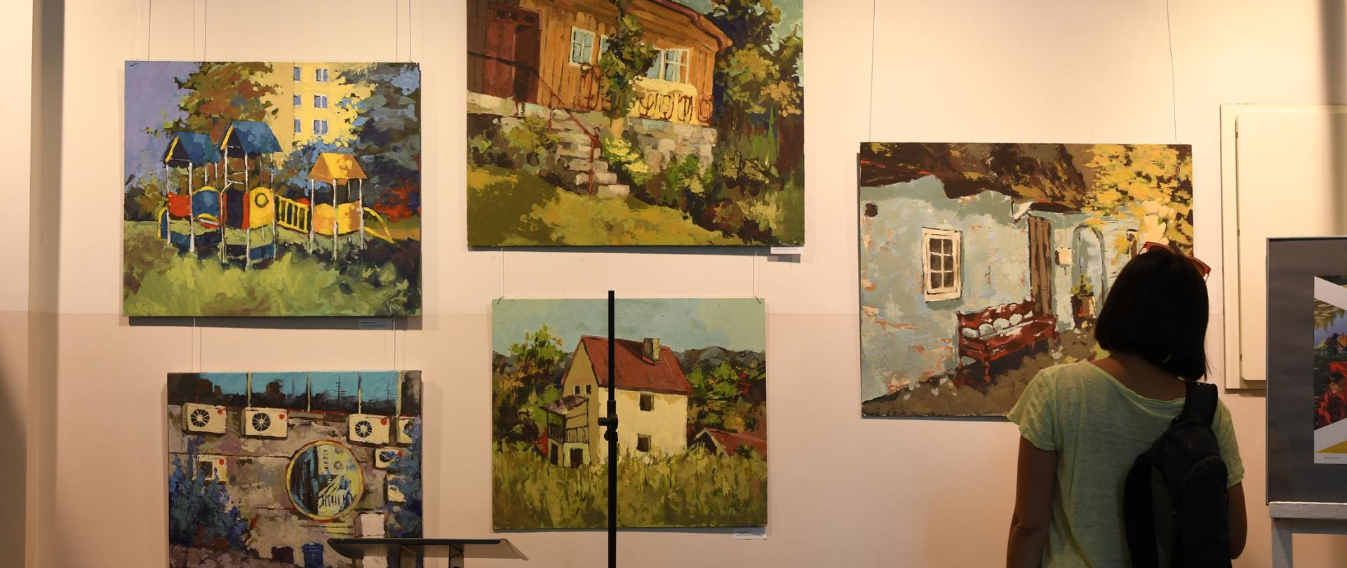 5 obrazów zawieszonych na ścianie galerii, przed obrazami stoi kobieta