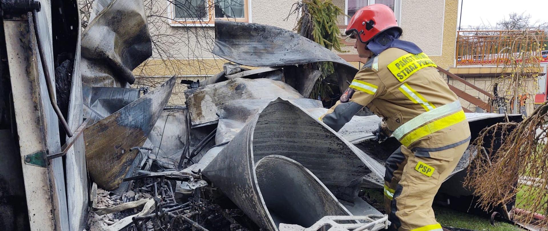 Strażak prowadzi działania na spalonych elementach, które pochodzą ze spalonego budynku. 