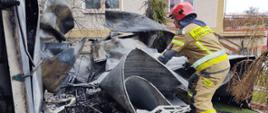 Strażak prowadzi działania na spalonych elementach, które pochodzą ze spalonego budynku. 