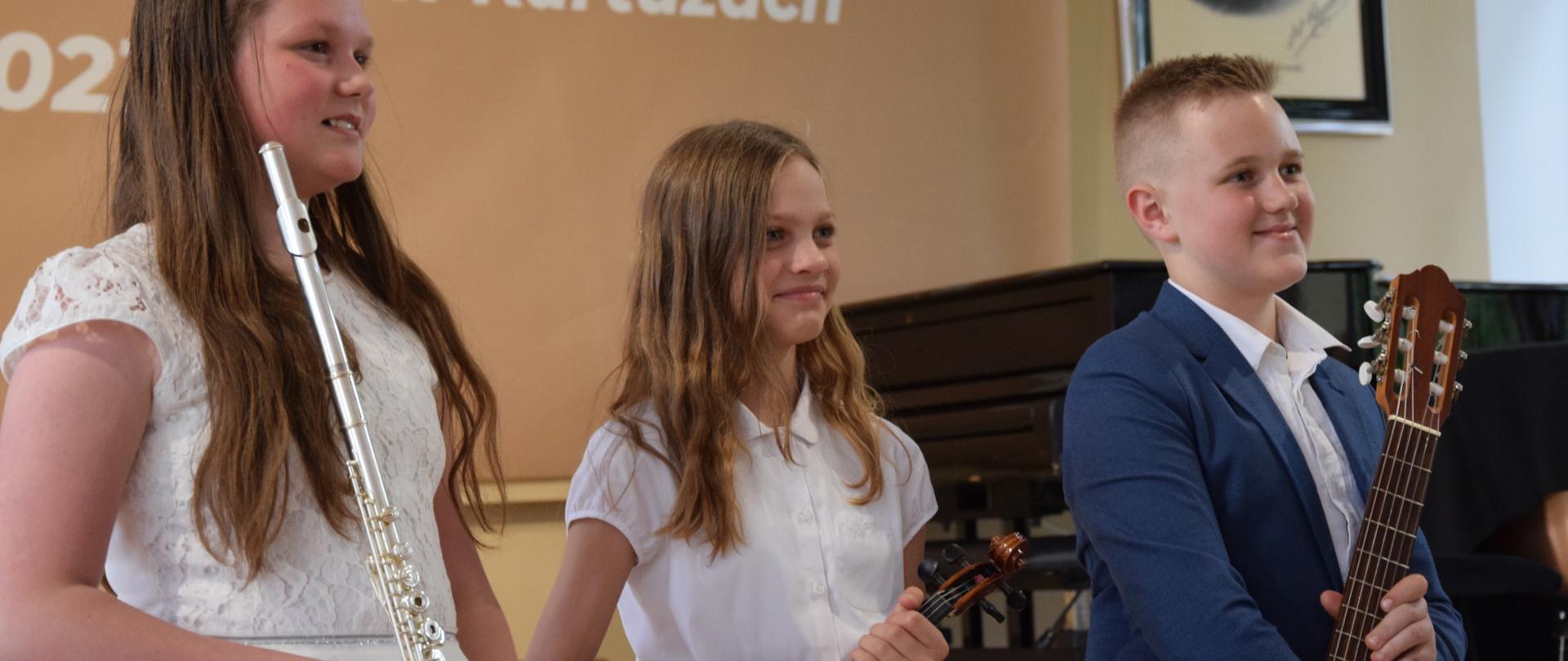 Uczniowie na scenie trzymający w rękach flet, skrzypce i gitarę