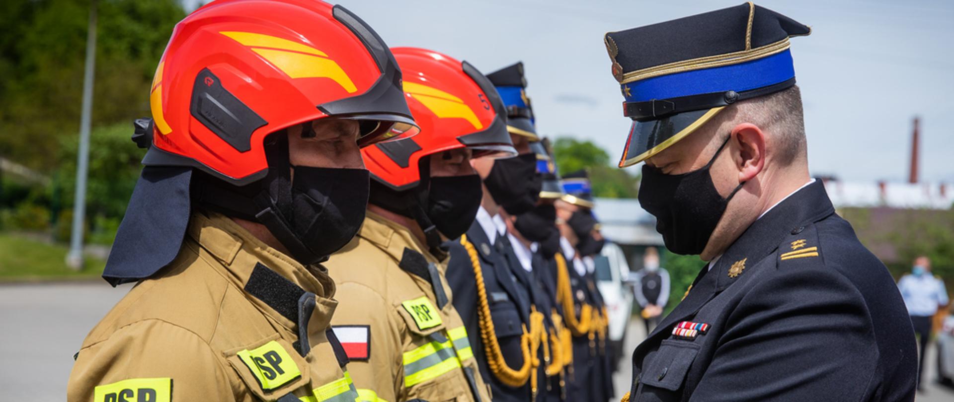 Na zdjęciu widoczni Z-ca Małopolskiego Komendanta Wojewódzkiego PSP wręczający strażakowi odznaczenie. Komendant w galowym granatowym mundurze i w czapce rogatywce. Strażak odbierający odznaczenie w piaskowym ubraniu specjalnym i czerwonym hełmie.