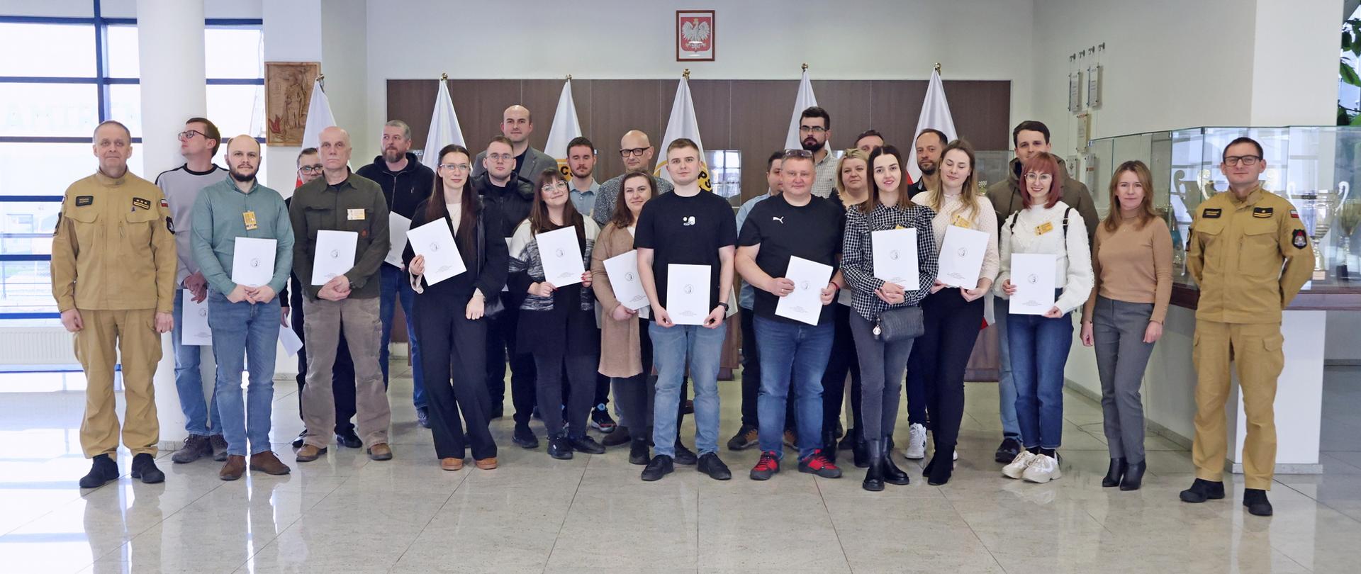 Pamiątkowe zdjęcie grupowe uczestników szkolenia inspektorów ochrony przeciwpożarowej (23 osoby) w towarzystwie dwóch funkcjonariuszy CS PSP oraz kobiety