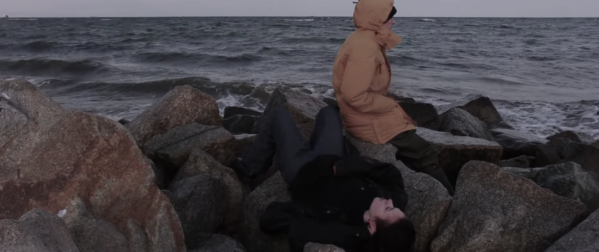 Kadr z filmu Nereida. Dwie postaci na kamienistym / skalistym brzegu morskim.