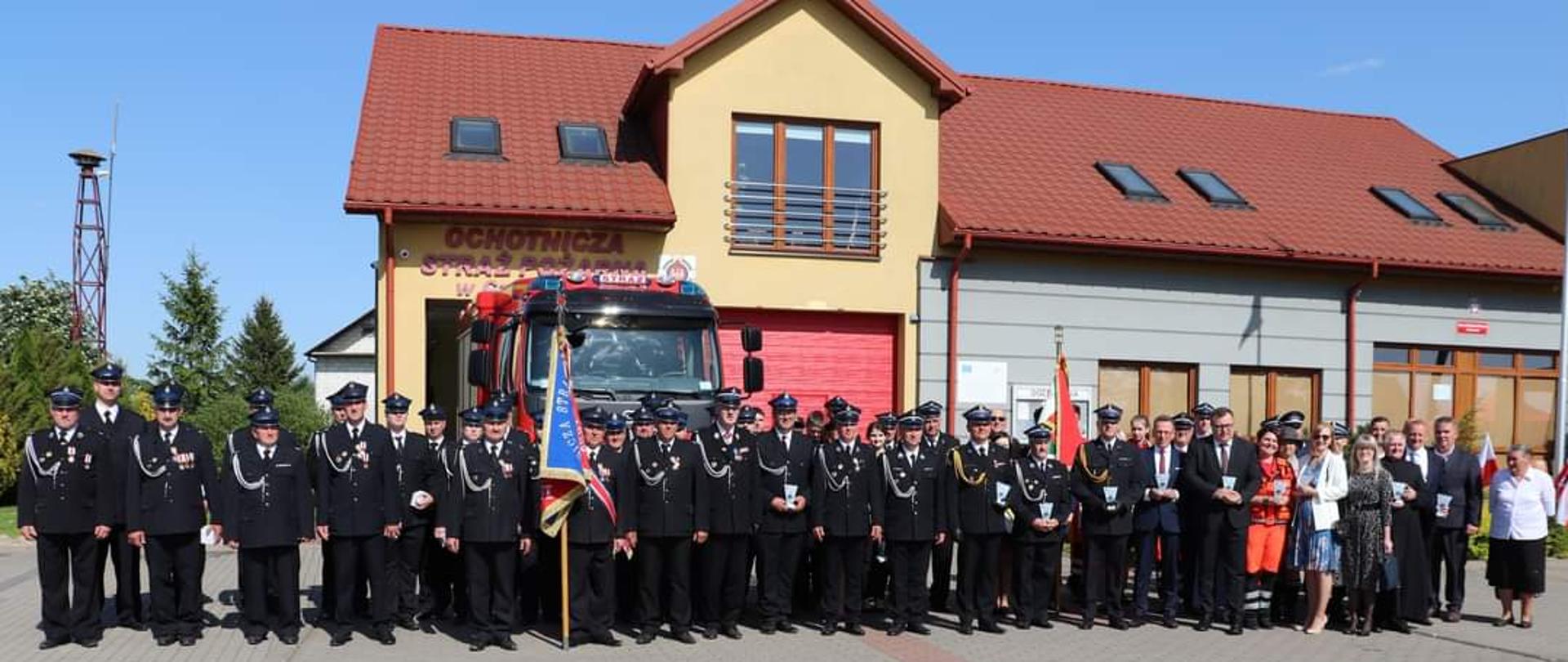 Na zdjęciu widać zgromadzonych strażaków ze sztandarem zgromadzonych przed strażnicą OSP z okazji uroczystość 100-lecia istnienia jednostki Ochotniczej Straży Pożarnej w Czerwonem