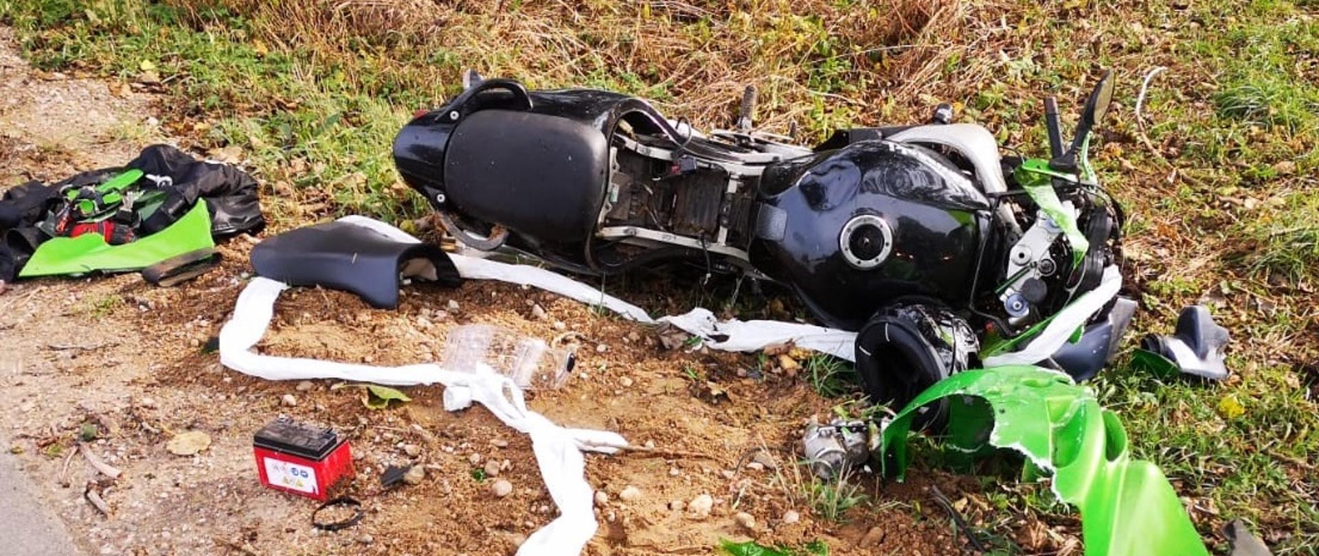 Rozbity czarno-zielony motocykl znajdujący się w przydrożnym rowie. 