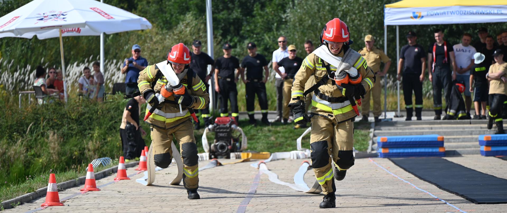 Strażacy rozwijają linię gaśniczą złożoną z węży pożarniczych na dwóch torach