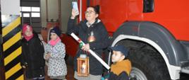Na tle wozu strażackiego stoją 3 druhny i druh ZHP. Najstarsza z nich w jednej ręce trzyma kalendarz, lampion oraz znicz. W drugiej - telefon komórkowy, którym wykonuje zdjęcie. 