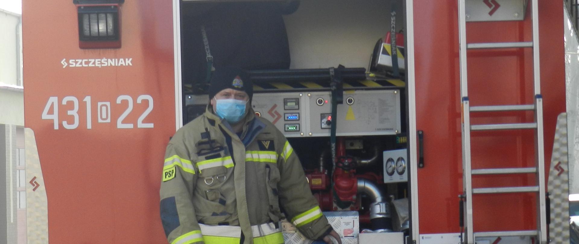 Zdjęcie przedstawia pojazd pożarniczy z operatorem autopompy umieszczonym na środku fotografii podczas ćwiczeń