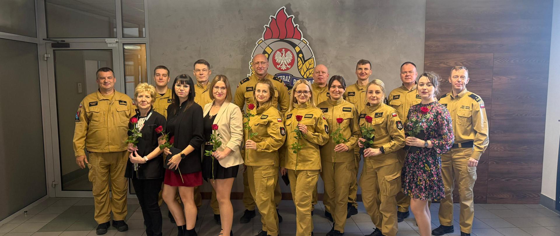 Obdarowane kwiatami panie, na nimi strażacy, w tle logo PSP