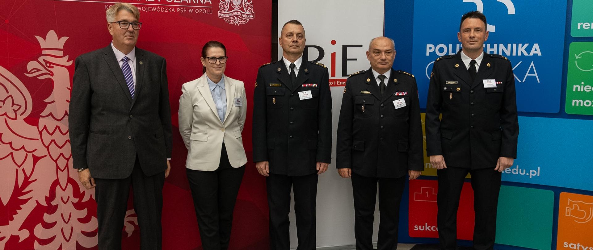 Od lewej stojący mężczyzna w garniturze, kolejno kobieta oraz trzech oficerów Państwowej Straży Pożarnej w umundurowaniu galowym na pamiątkowym zdjęciu