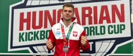 Zdjęcie przedstawia funkcjonariusza straży pożarnej w Kartuzach ubranego w dres reprezentacji Polski z zawieszonym medalem na szyi.