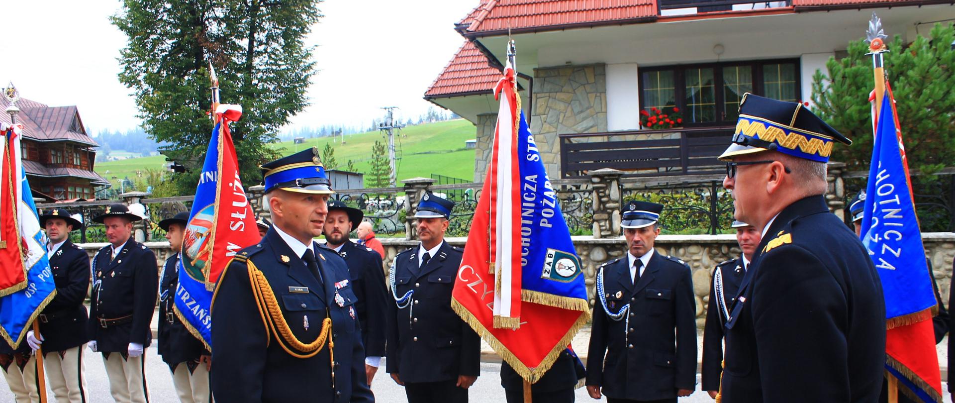 Dowódca uroczystości składa meldunek Zastępcy KG PSP , w tle poczty sztandarowe i budynek mieszkalny