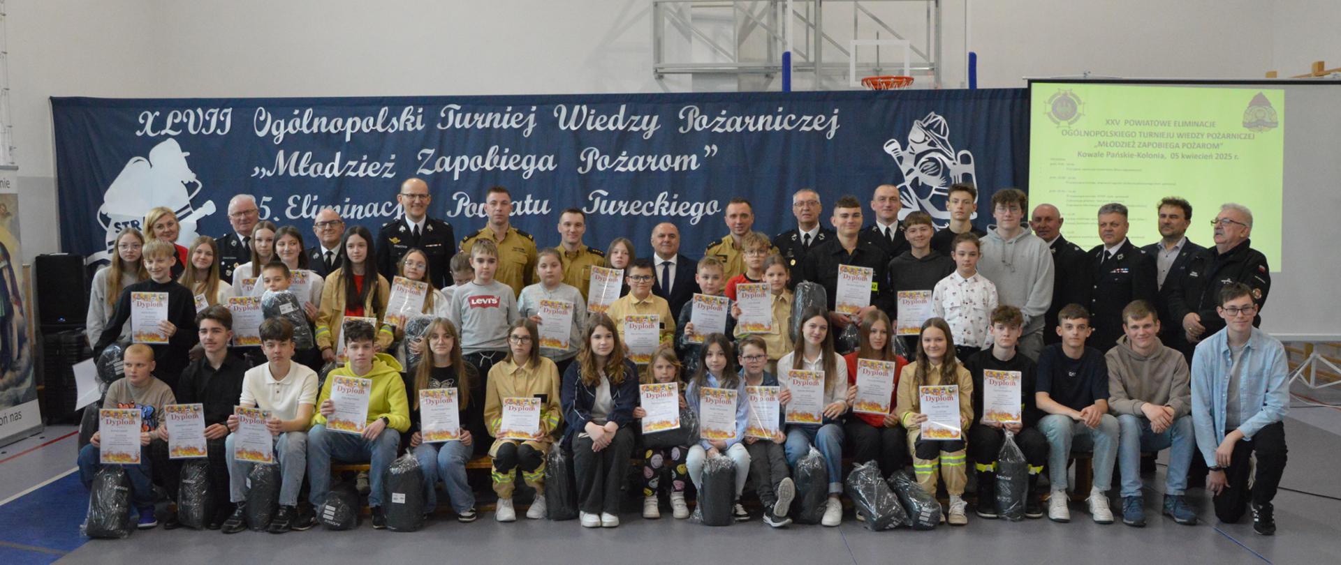 Uczestnicy konkursu pozują do zdjęcia trzymając w rękach dyplomy, z tyłu w ostatnim rzędzie stoją członkowie jury oraz organizatorzy konkursu. 