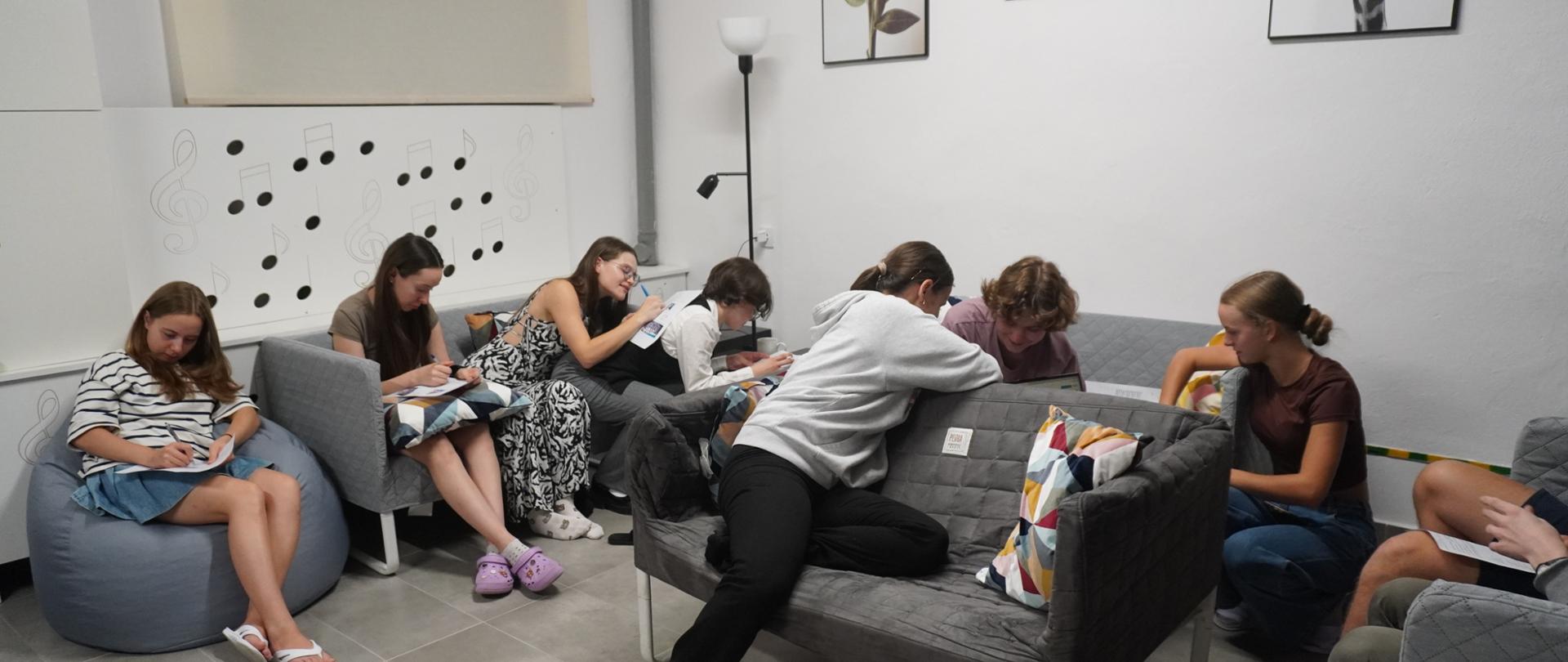 Wychowankowie siedzą na kanapach i pufach. Zaznaczają odpowiedzi na kartach konkursowych. 