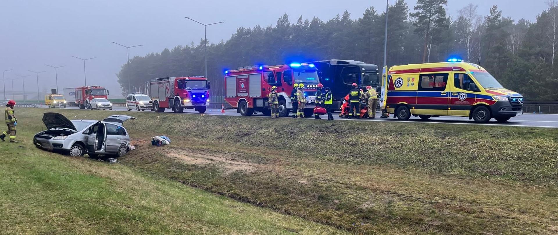 Samochód osobowy na pasie zieleni i działające służby