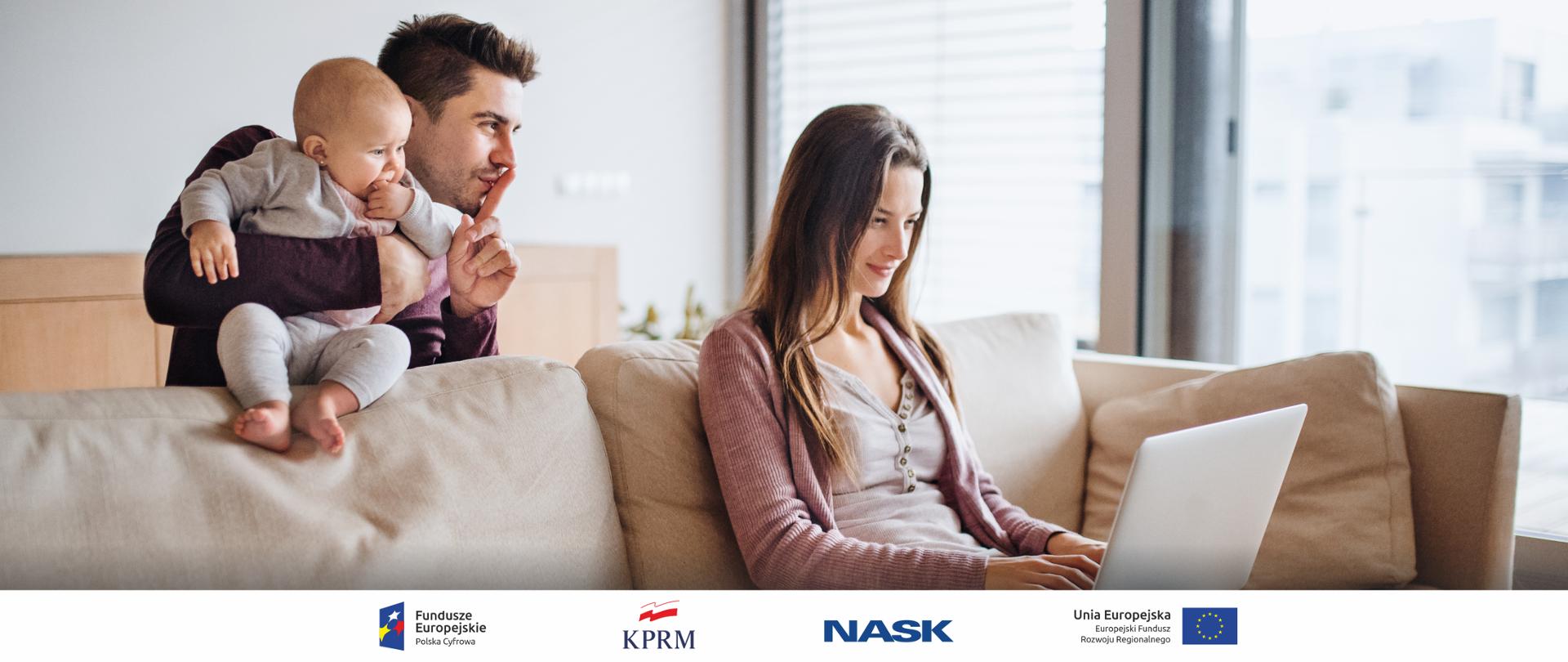 Zdjęcie, na którym widać młoda kobietę siedzącą na kanapie i korzystająca z laptopa. Za kanapą stoi mężczyzna, który trzyma na rękach małe dziecko. Przykłada palec do ust, „znak ciszy”.