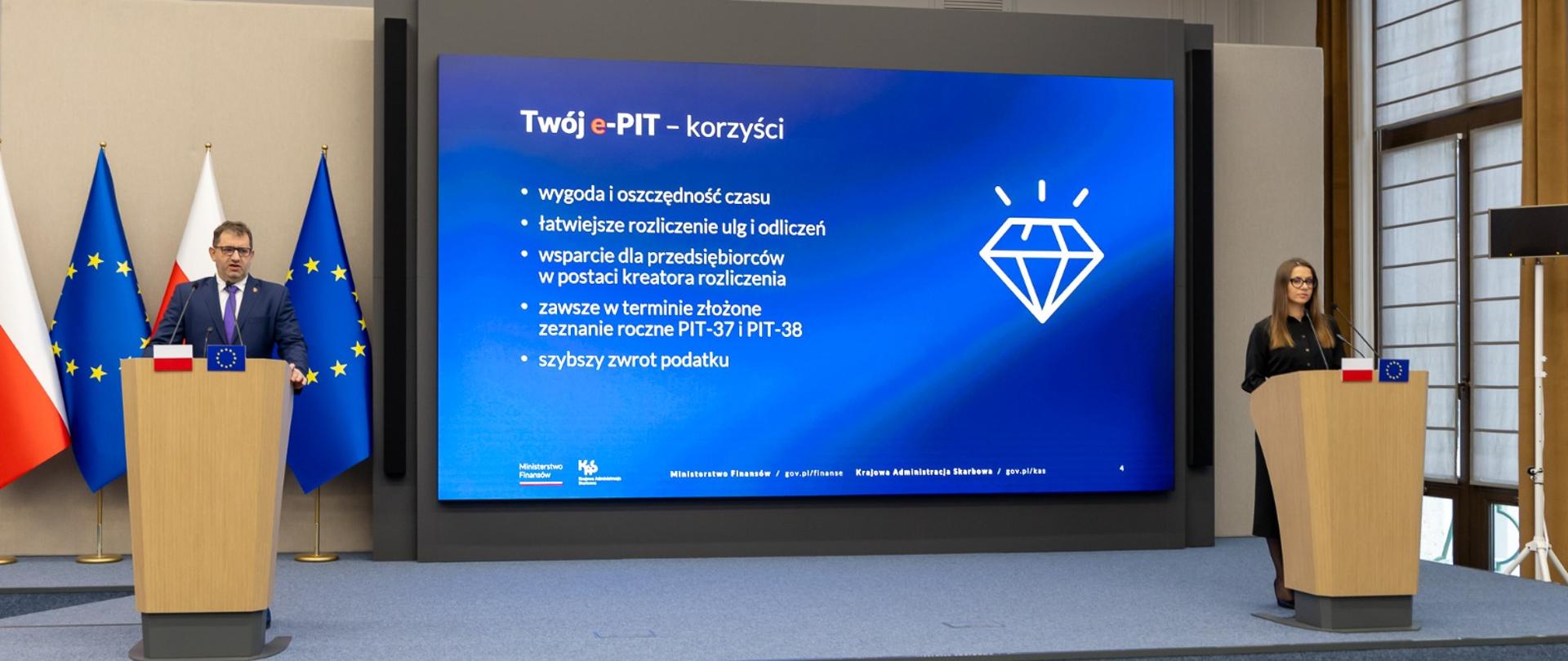 Po lewej przy mównicy Szef KAS Marcin Łoboda, po prawo przy mównicy Zastępca Szefa KAS Małgorzata Krok. Pomiędzy nimi wyświetlana jest prezentacja