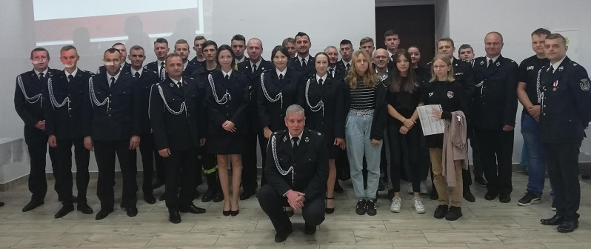 Fotografia przedstawia druhów OSP Dziecinów wraz z Komendantem Powiatowym PSP w Otwocku, st. bryg. Tomaszem Królem, podczas zebrania walnego. Umundurowanie wyjściowe.