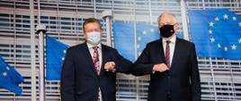 Wicepremier, minister rozwoju, pracy i technologii Jarosław Gowin w maseczce na twarzy, po jego lewej stronie stoi Wiceprzewodniczący KE Maroš Šefčovič. Obaj politycy witają się łokciami. Z tyłu flagi UE.