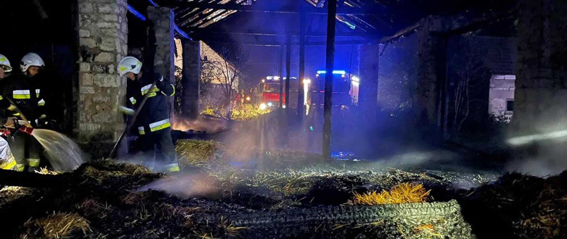 Zdjęcie przedstawia palącą się stodołę oraz strażaków podczas działań gaśniczych.