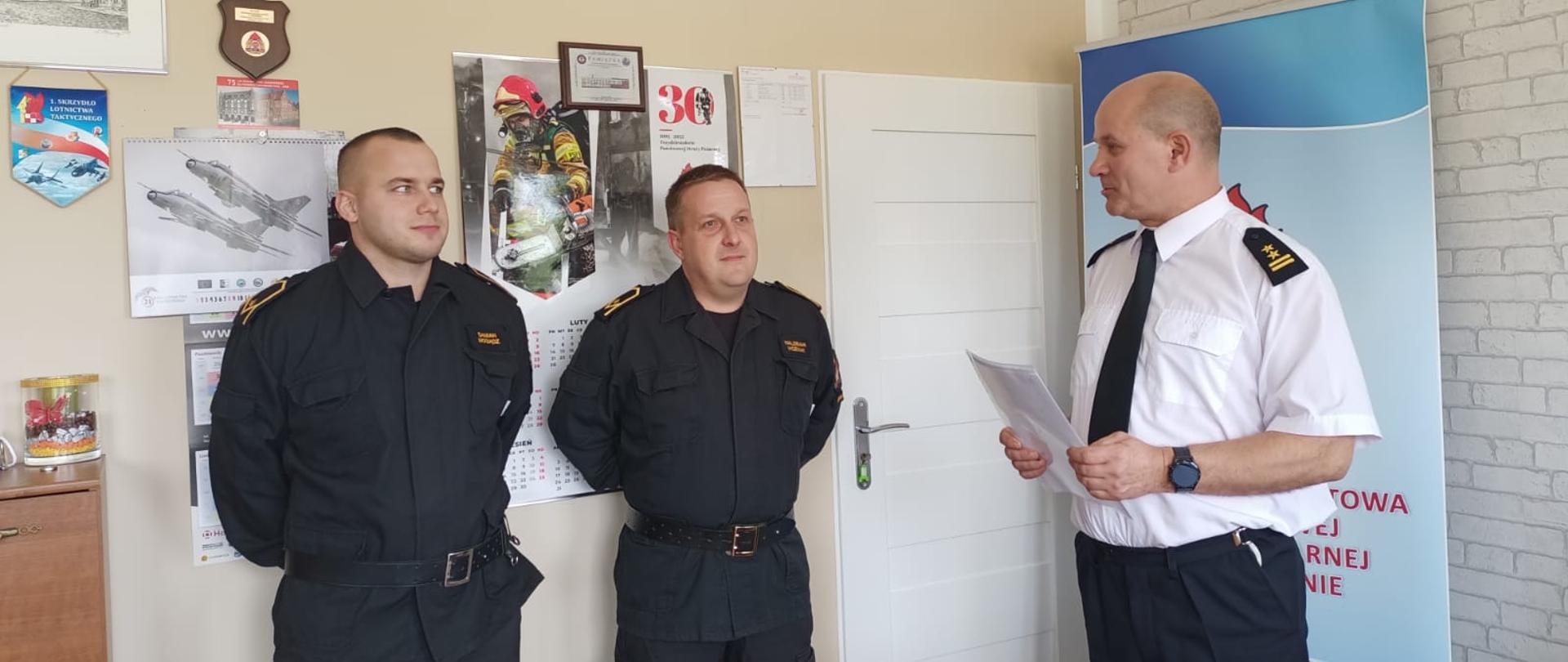 Zdjęcie przedstawia trzech strażaków w biurze podczas wręczania awansów na wyższe stanowiska służbowe.