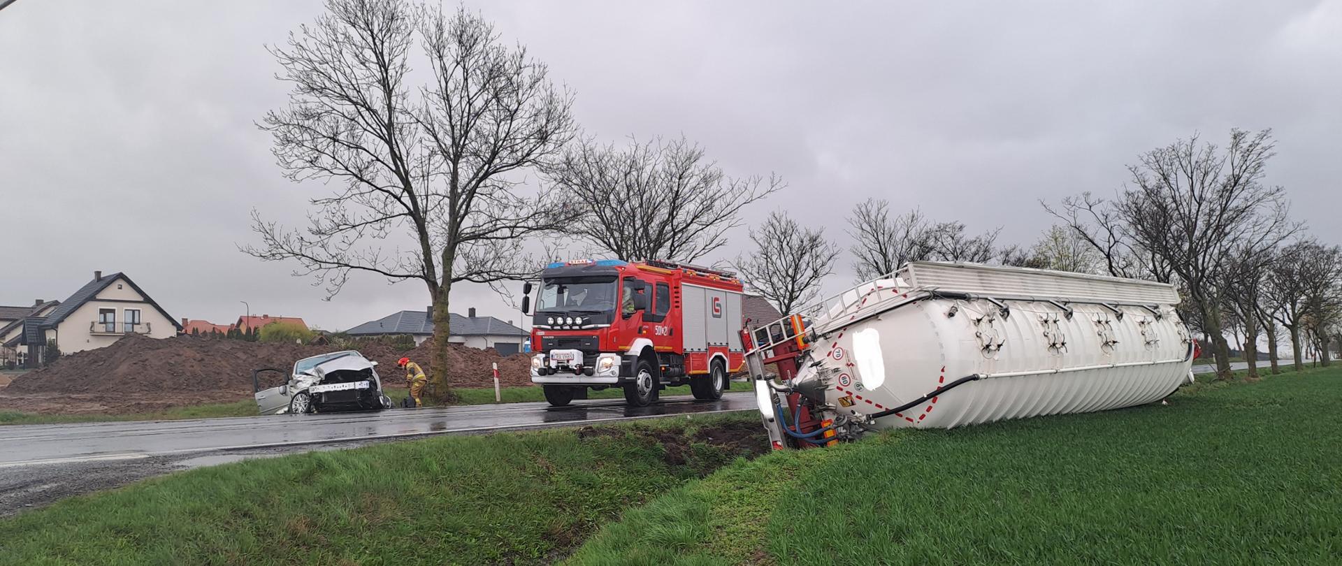 Zdjęcie przedstawia samochód cysternę oraz samochód osobowy po wypadku drogowym, na drugim planie wóz strażacki