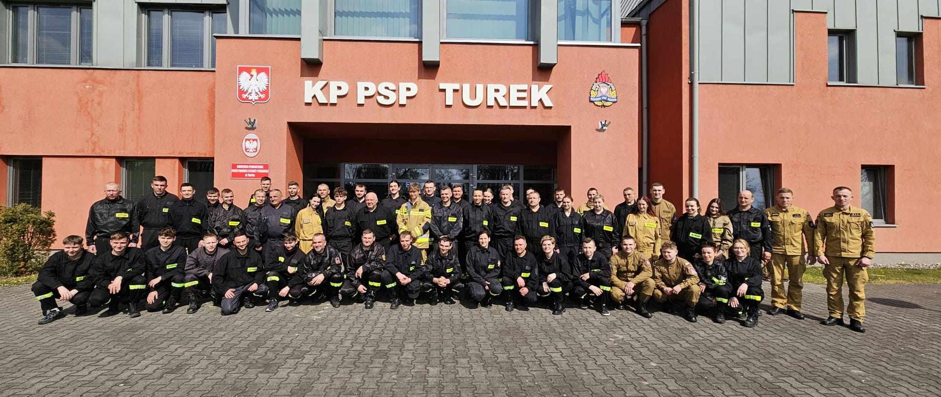 Uczestnicy szkolenia pozują do zdjęcia przed budynkiem Komendy Powiatowej Państwowej Straży Pożarnej w Turku wraz z prowadzącymi zajęcia. 
